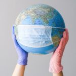 hands with latex gloves holding a globe with a face mask